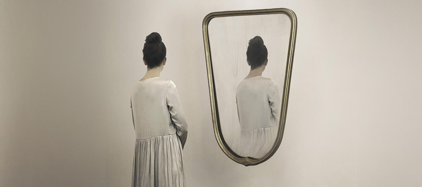 A woman looking at a half length mirror only to see her reflection facing away from her 